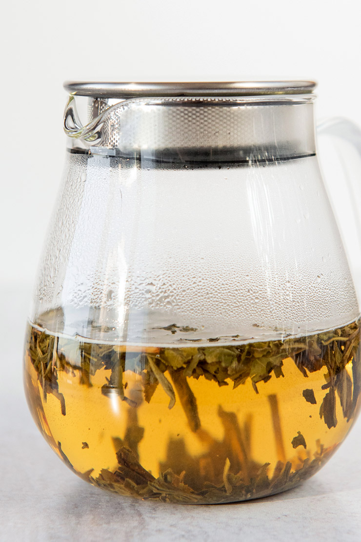 Loose tea steeping in a covered glass teapot.