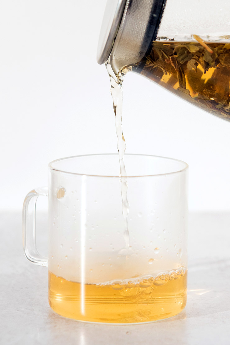 Pouring hot jasmine tea into a glass mug from a teapot.