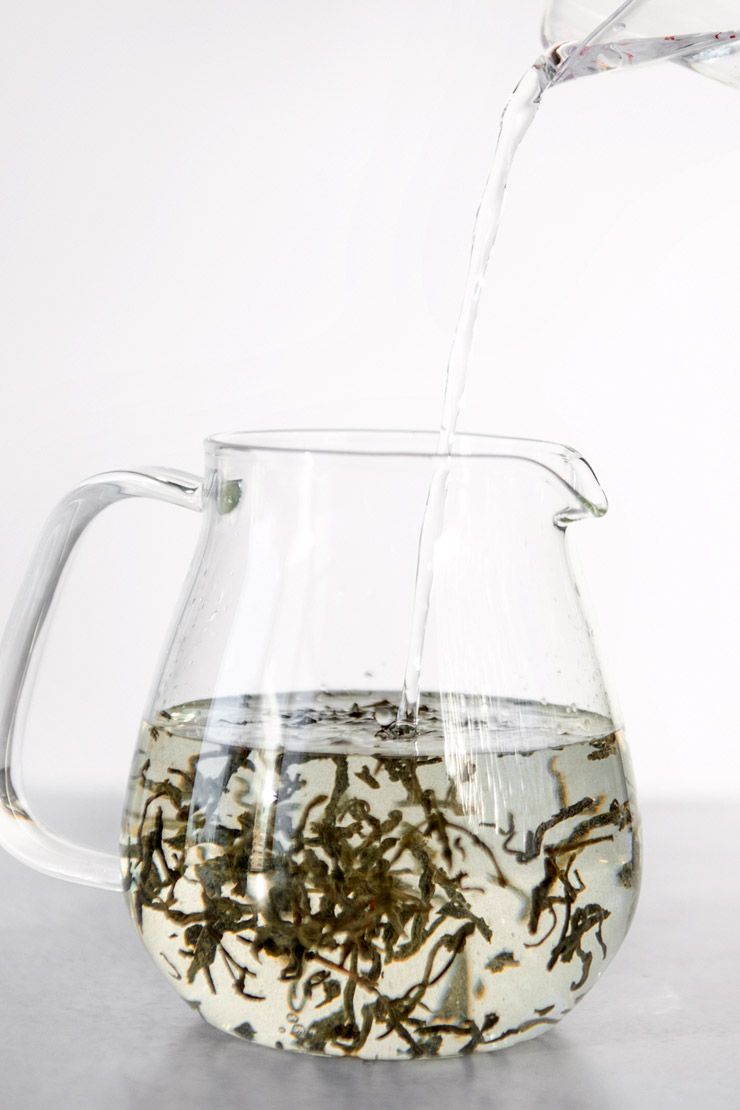 Pouring cool water into a glass teapot with jasmine tea.