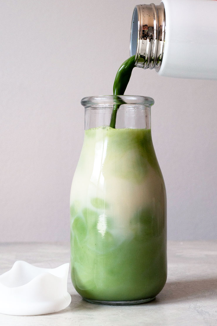 Pouring matcha into a milk bottle with oat milk.