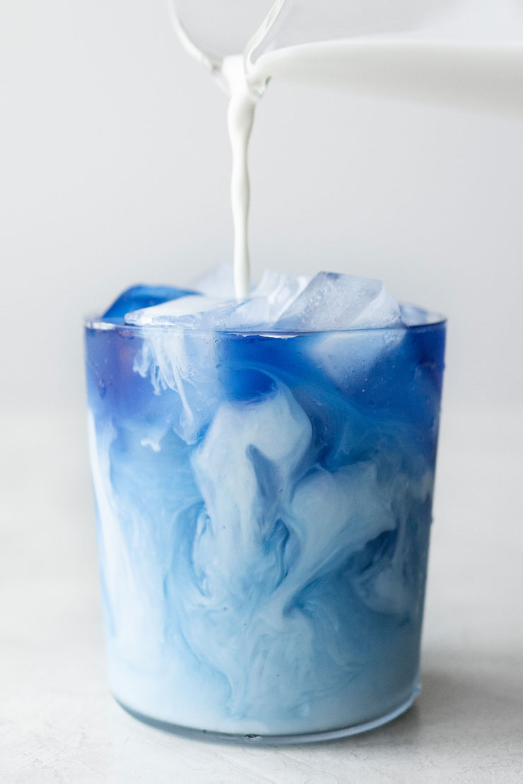 Pouring milk into an Iced Butterfly Pea Flower Tea Latte.
