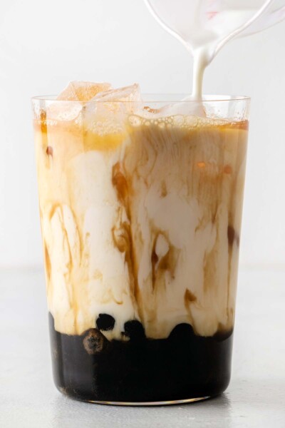 Pouring milk into a cup with black tea and boba. 