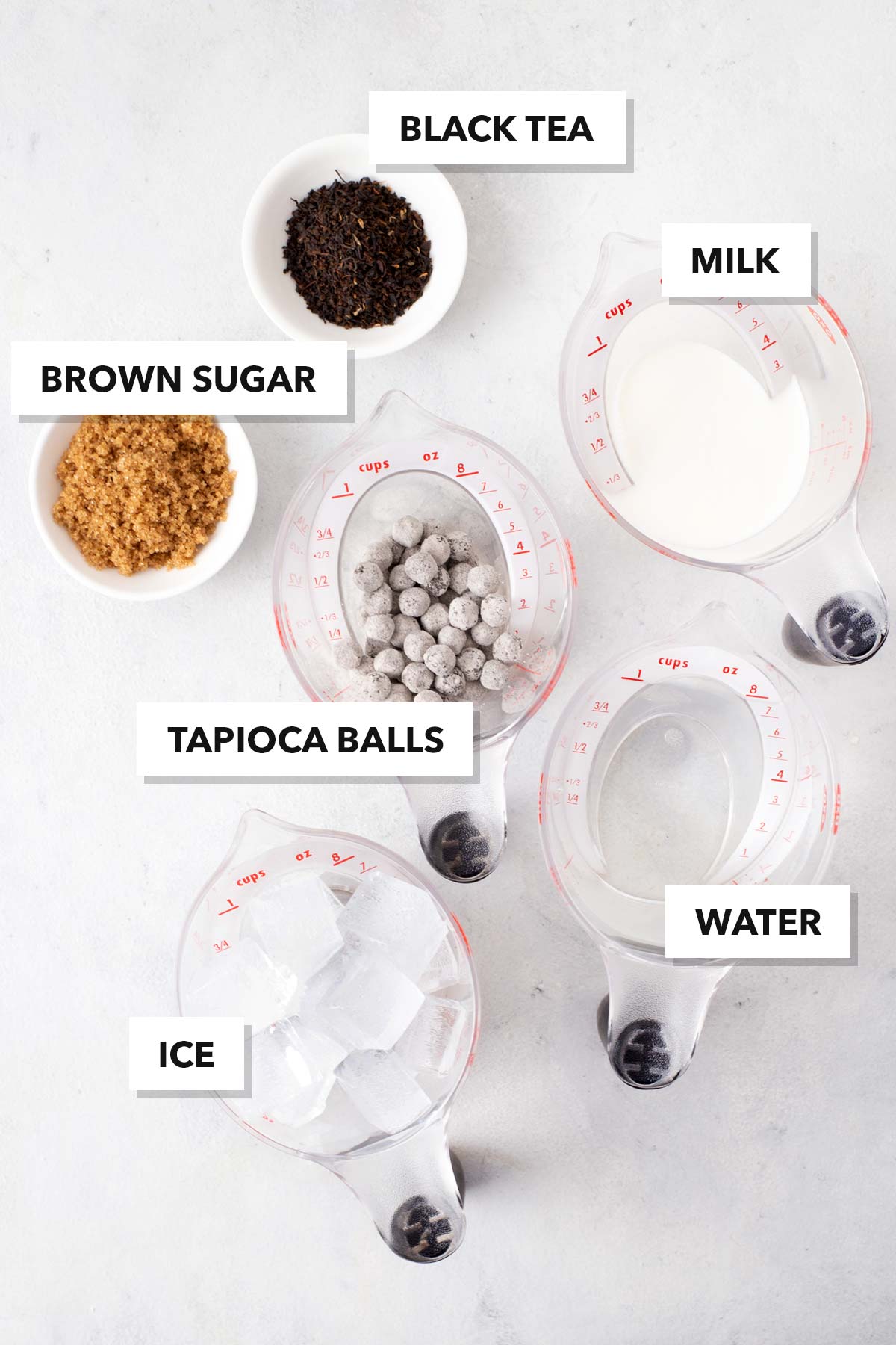 Bubble Tea or Boba Milk Tea ingredients on a table in measuring bowls and cups with labels.
