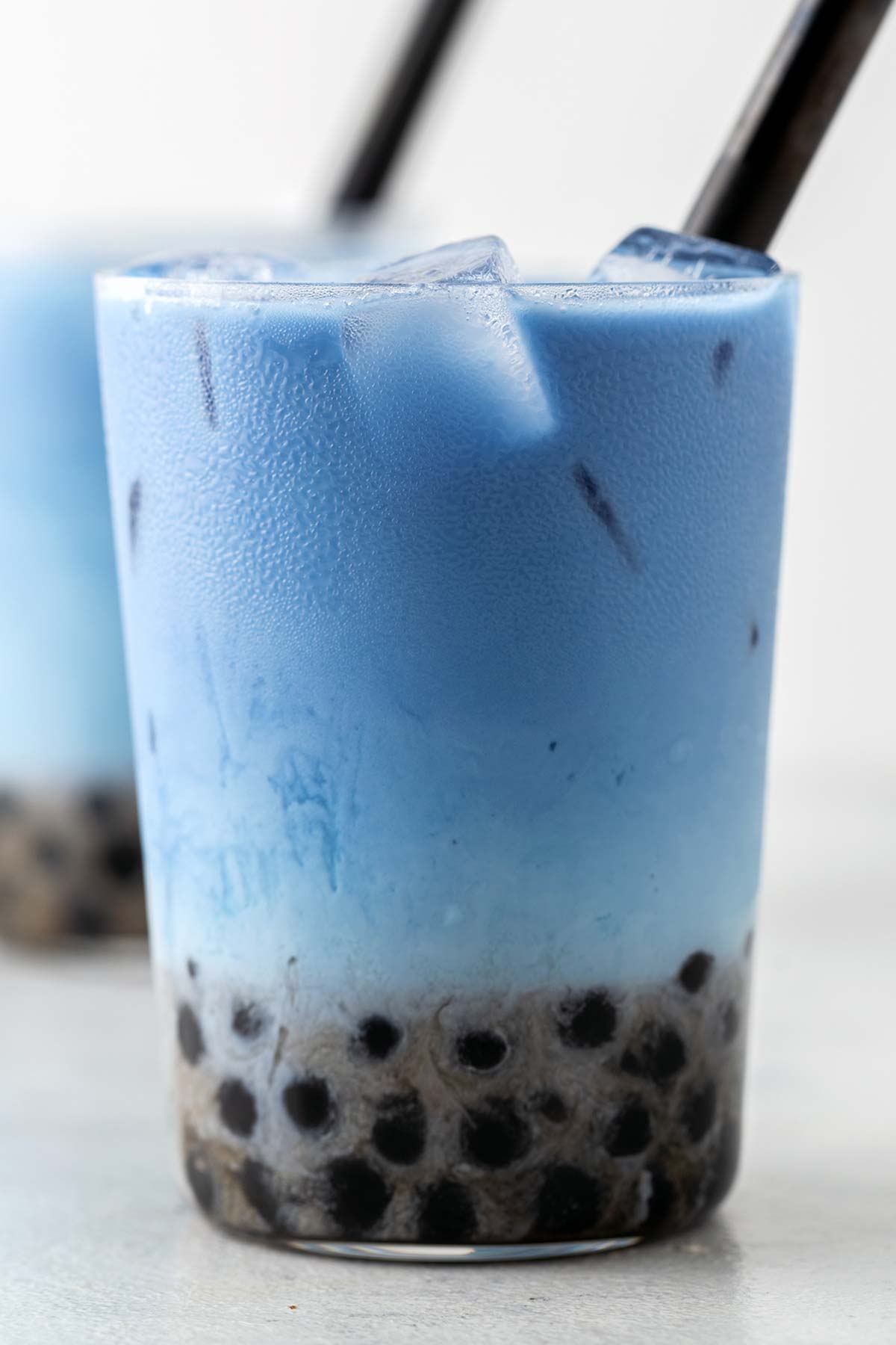 A Butterfly Pea Flower Bubble Tea (Butterfly Pea Flower Milk Tea with Boba) in a clear glass with a wide straw and boba at the bottom.