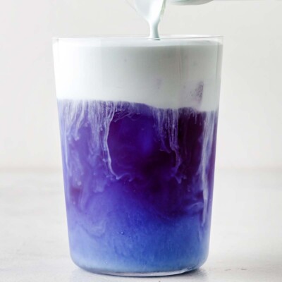 Butterfly Pea Flower Cold Foam being poured into clear glass on top of Butterfly Pea Flower Iced Tea.