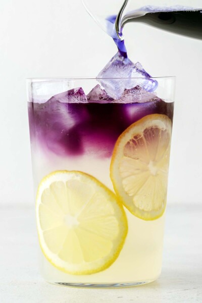 Pouring butterfly pea flower tea into a cup with lemonade and ice. 