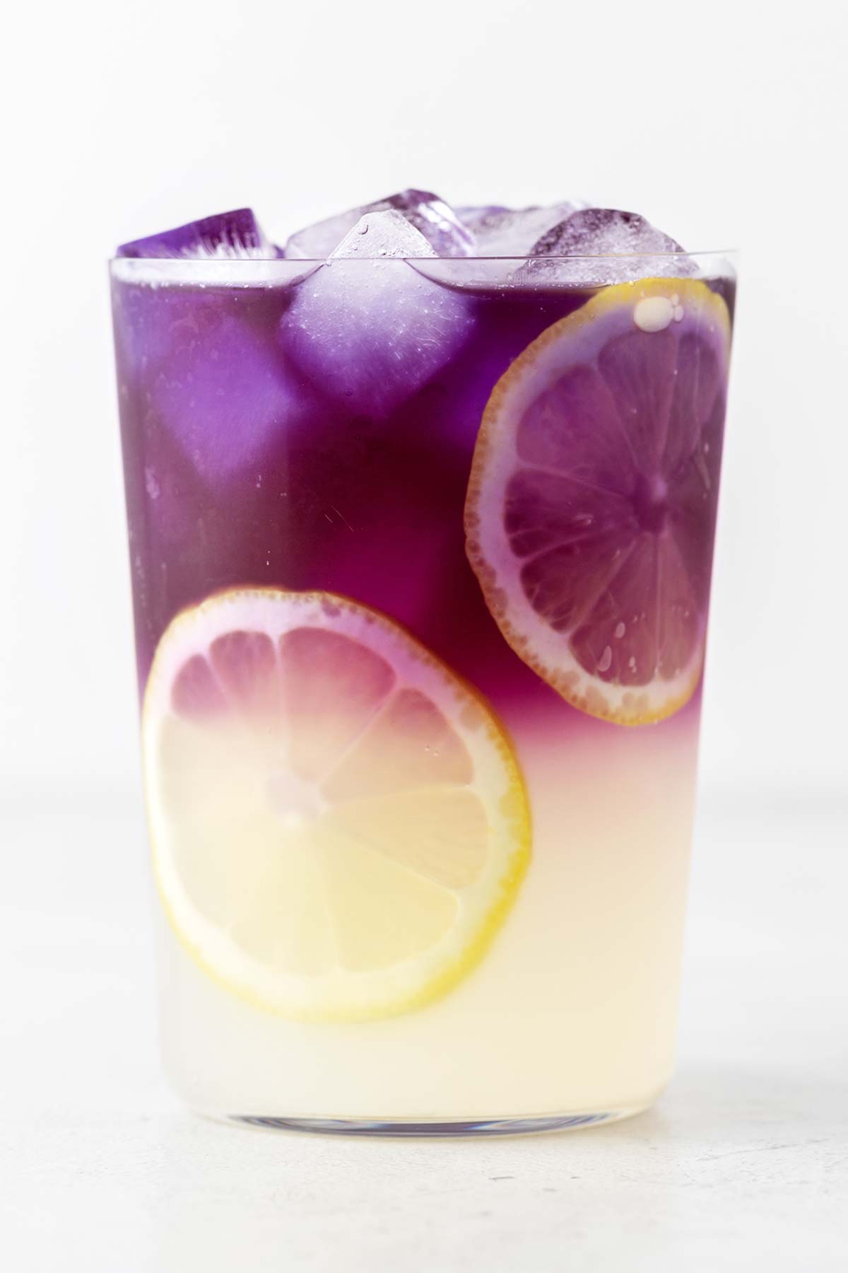 Butterfly Pea Flower Lemonade in a glass garnished with lemon slices.