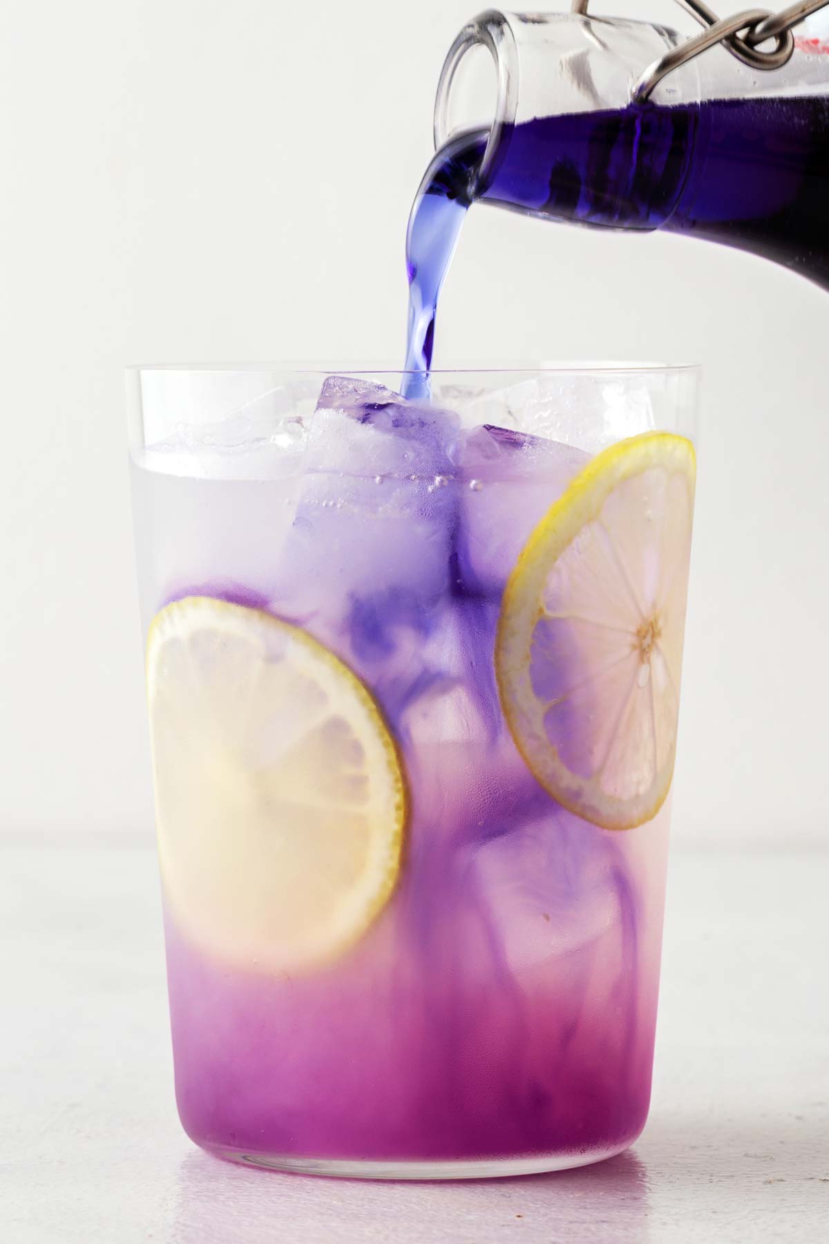Butterfly Pea Flower Syrup being poured into clear glass with lemonade.