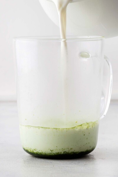 Pouring heated milk into a cup with matcha powder. 
