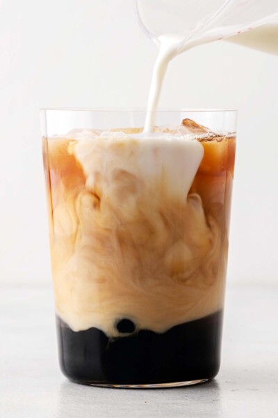 Pouring milk into a cup with tea, boba, and ice. 