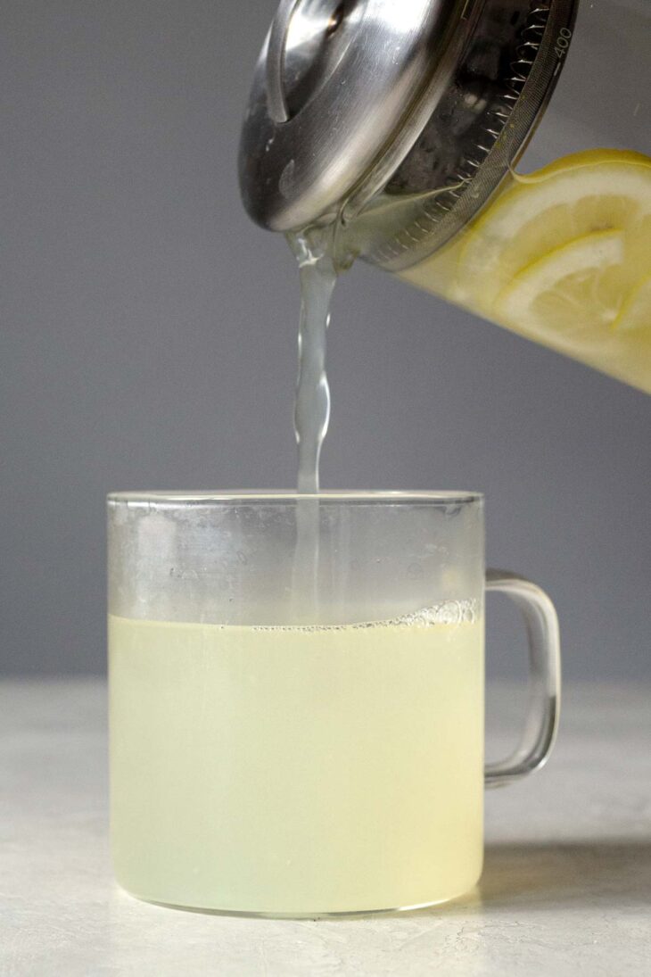 Pouring ginger tea into a glass mug.