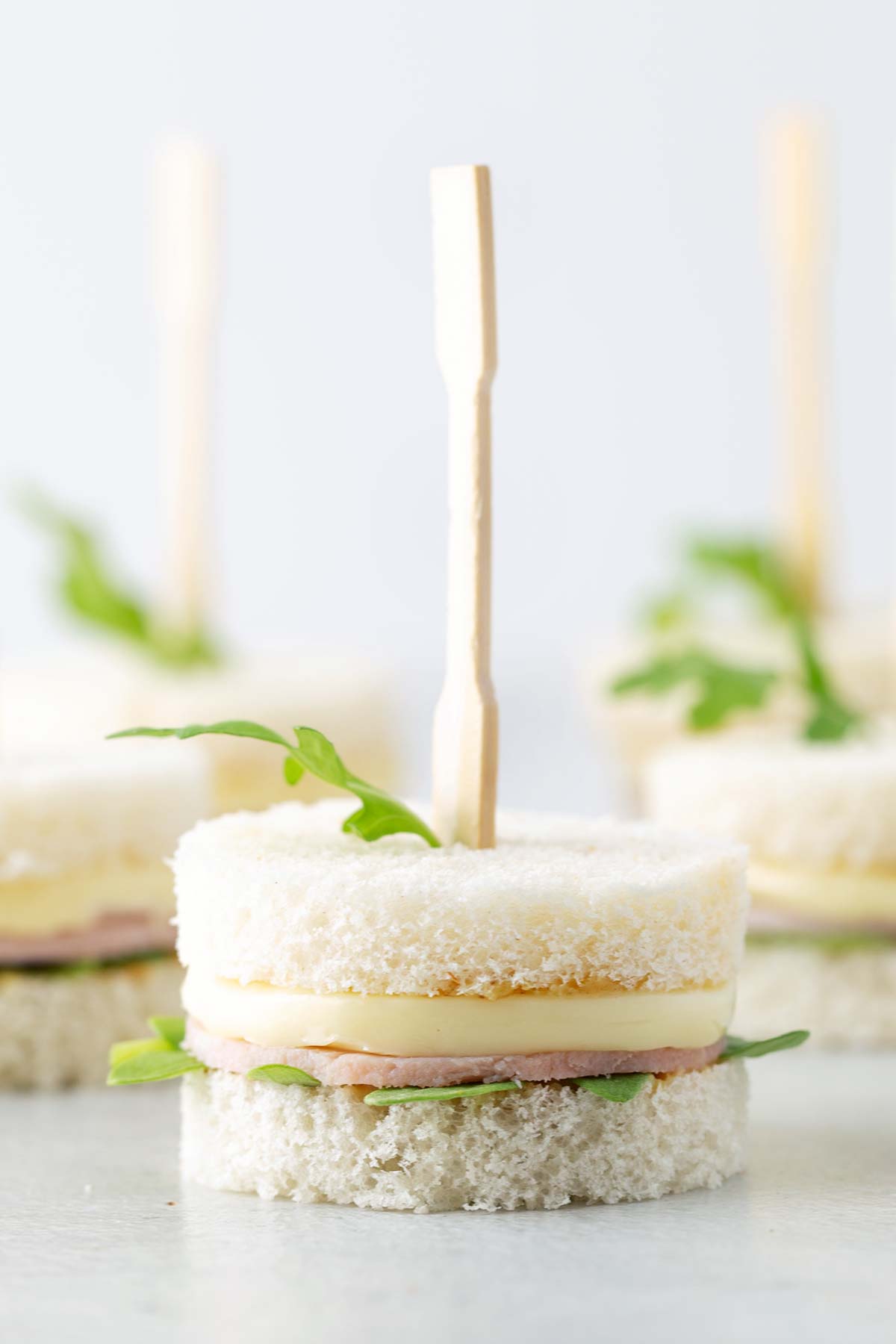 Close up of Ham & Brie Tea Sandwiches held together by cocktail fork.