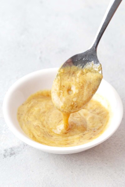 Spoon mixing together honey and mustard in small white bowl.