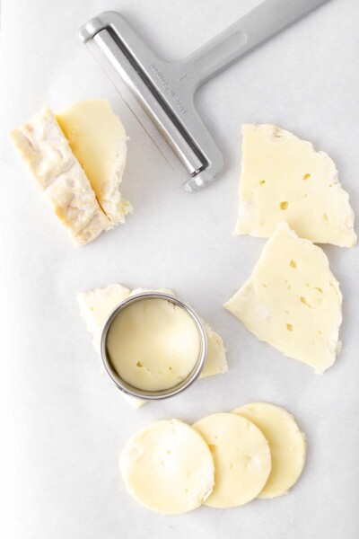 Brie being sliced with cheese slice and cut into circles with cookie cutter.