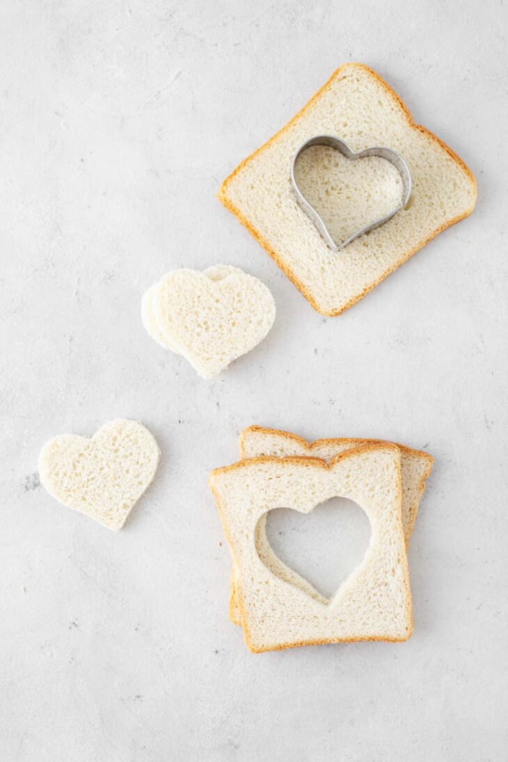 Cutting hearts out of white bread slices with a heart-shaped cookie cutter.