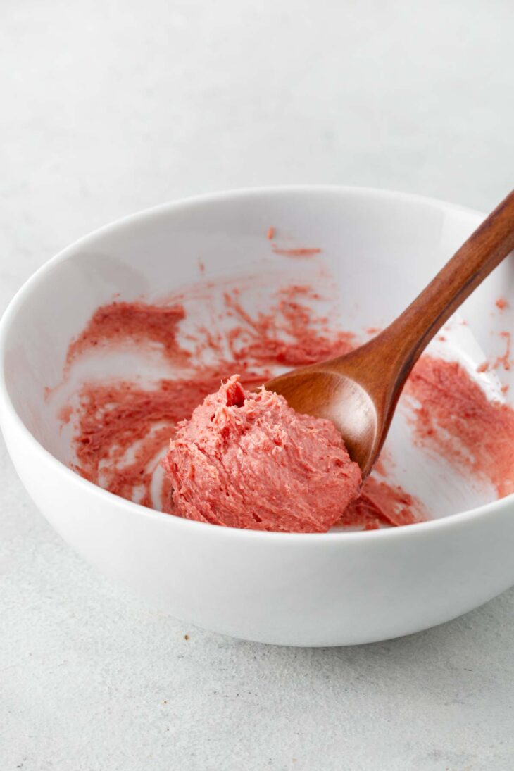 Strawberry cream cheese in a white bowl with a wooden spoon.