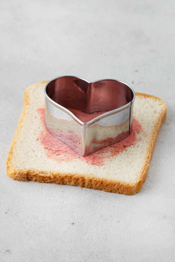 Heart cookie cutter on a slice of bread with strawberry cream cheese.