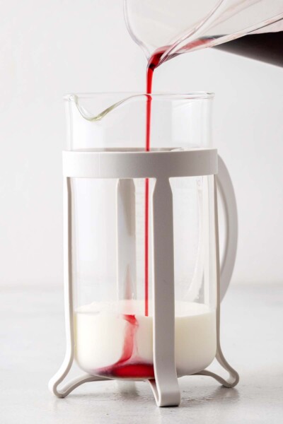 Pouring hibiscus syrup into a French press with milk.