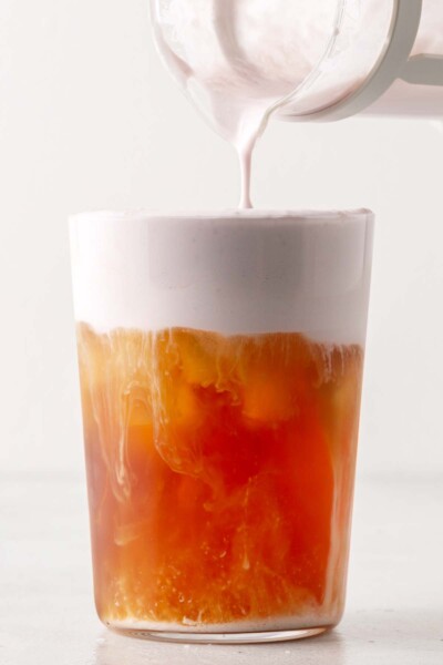 Pouring hibiscus cold foam onto tea.