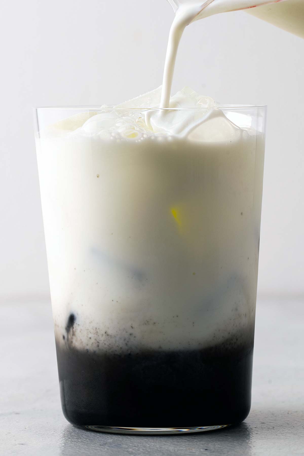 Milk being poured into Iced Black Sesame Latte in clear glass.