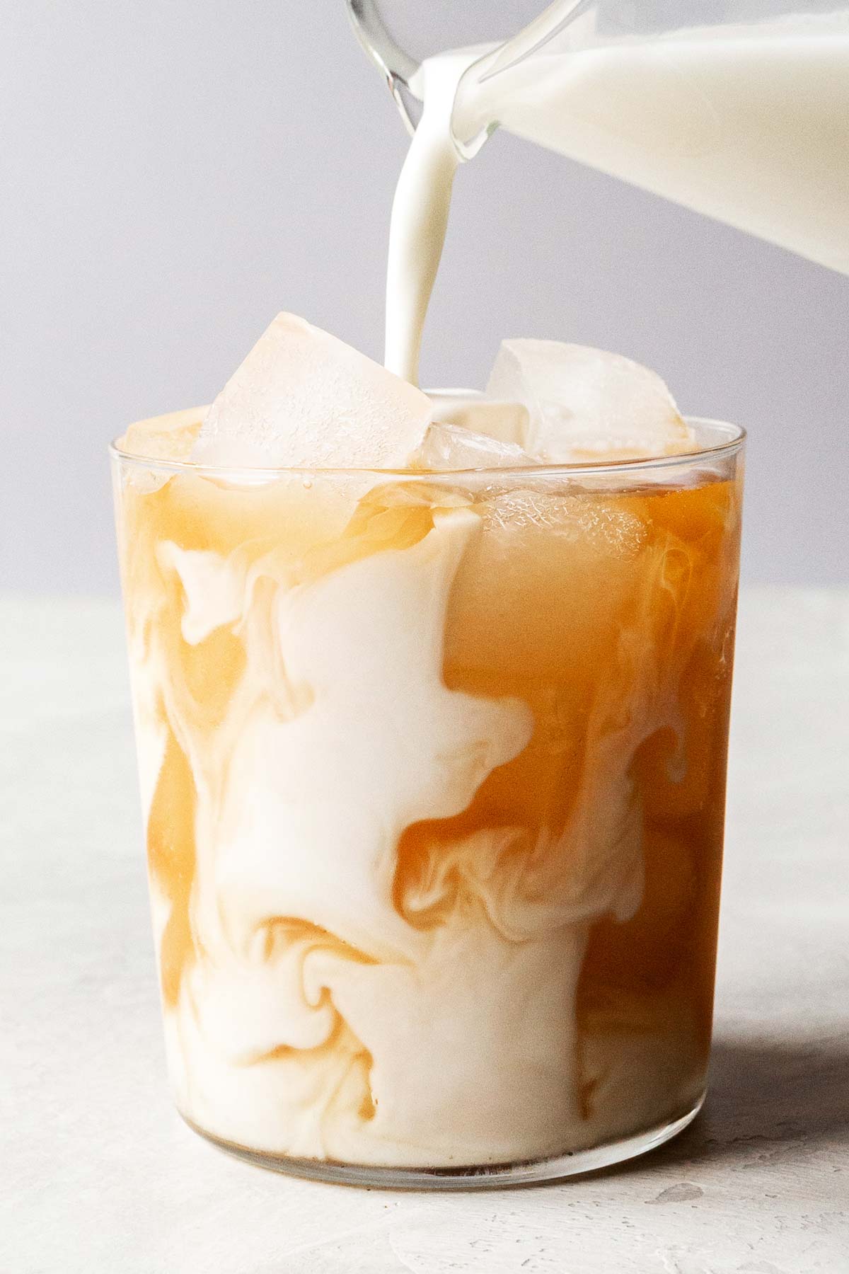 Pouring milk into a cup with Iced Chai Latte.