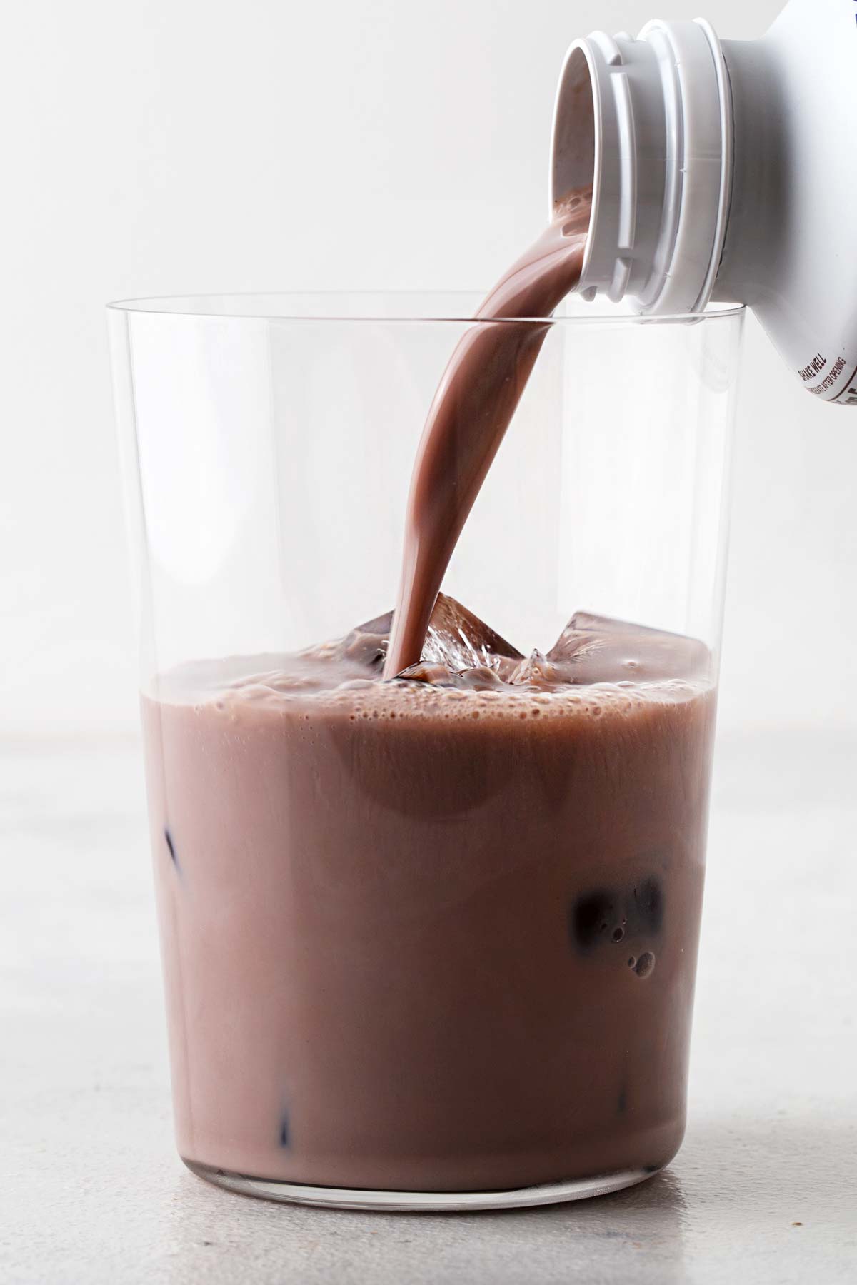 Pouring chocolate protein shake in a glass with ice.