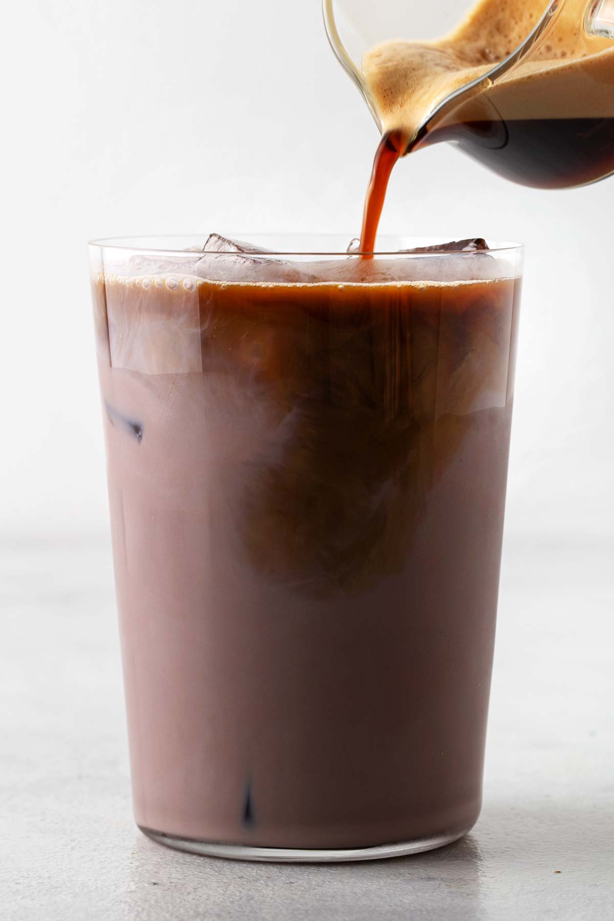 Pouring espresso in a glass with chocolate protein shake and ice.