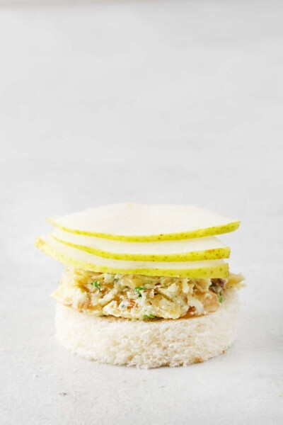 Sliced pears placed on top of blue cheese mixture on white bread.
