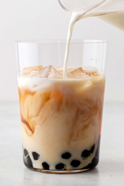 Pouring milk into a cup with tea, boba, and ice. 