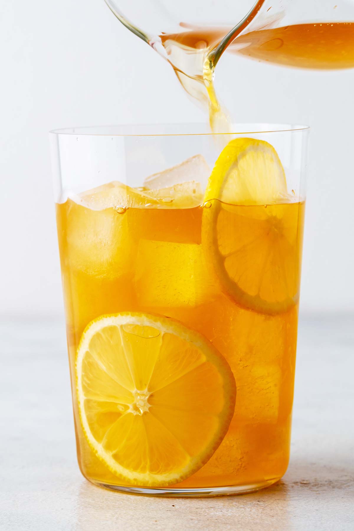 Pouring Lemon Iced Tea into a cup garnished with lemon slices.