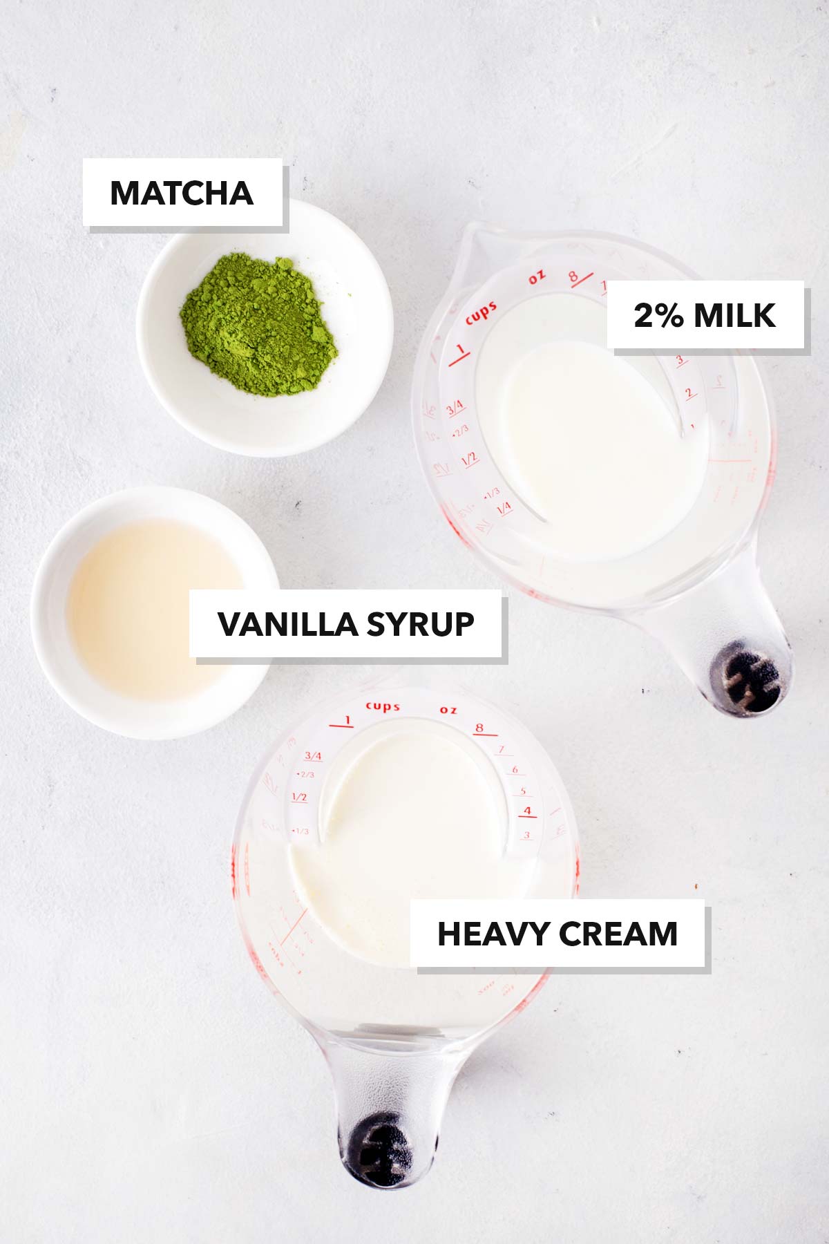 Easy matcha cold foam ingredients in measuring cups, and labeled, on a table.