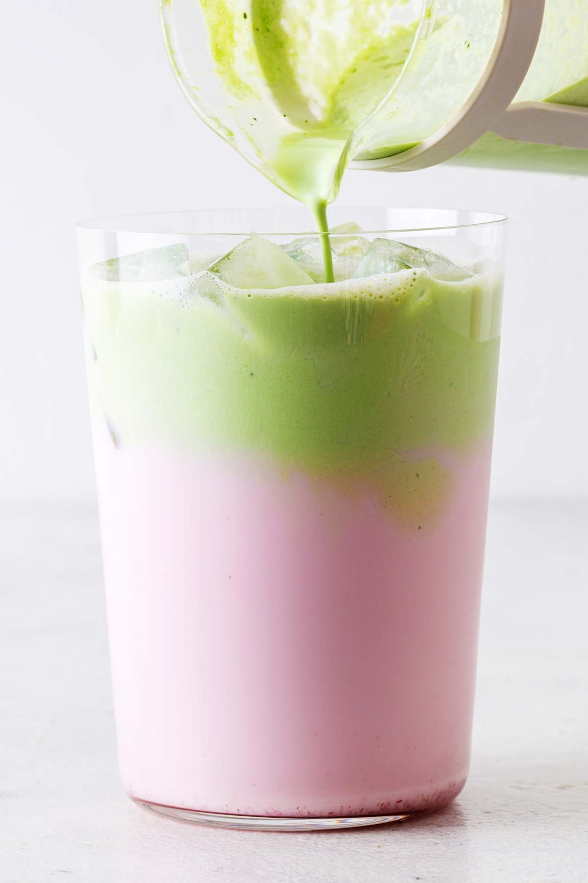 Pouring matcha cold foam on top of strawberry milk.