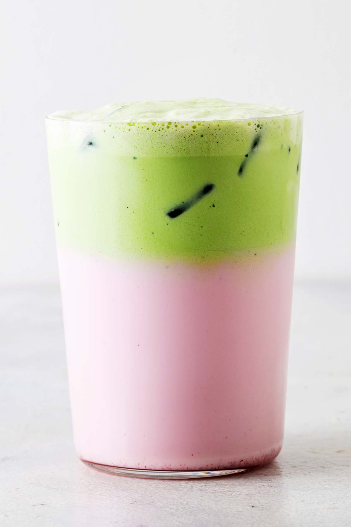 Easy matcha cold foam already poured over a pink iced latte in a clear glass.
