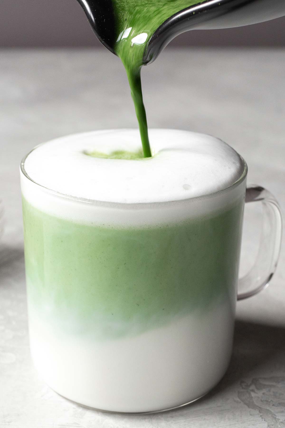 Pouring matcha into a glass of frothed milk.