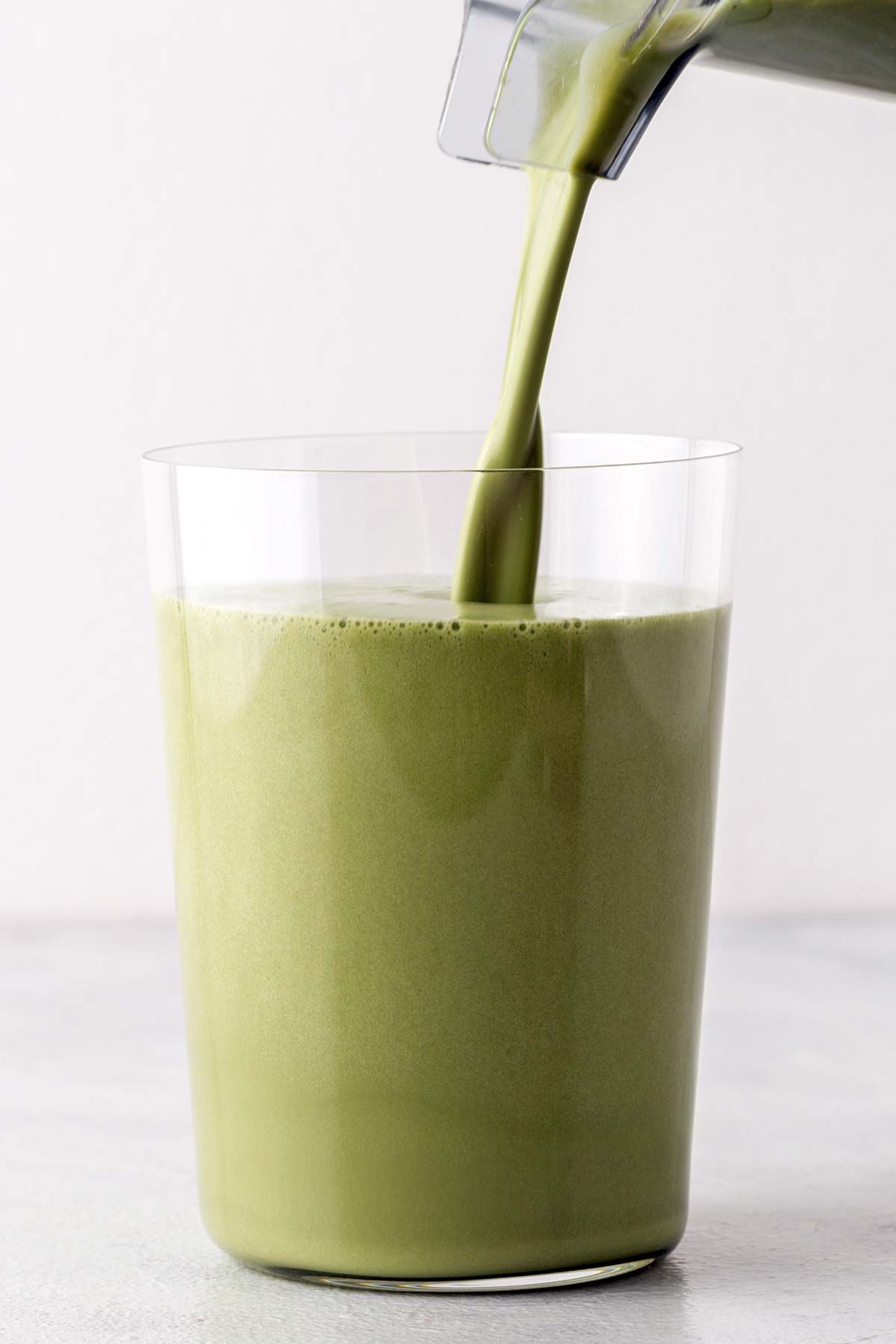 Matcha protein shake being poured into a cup.