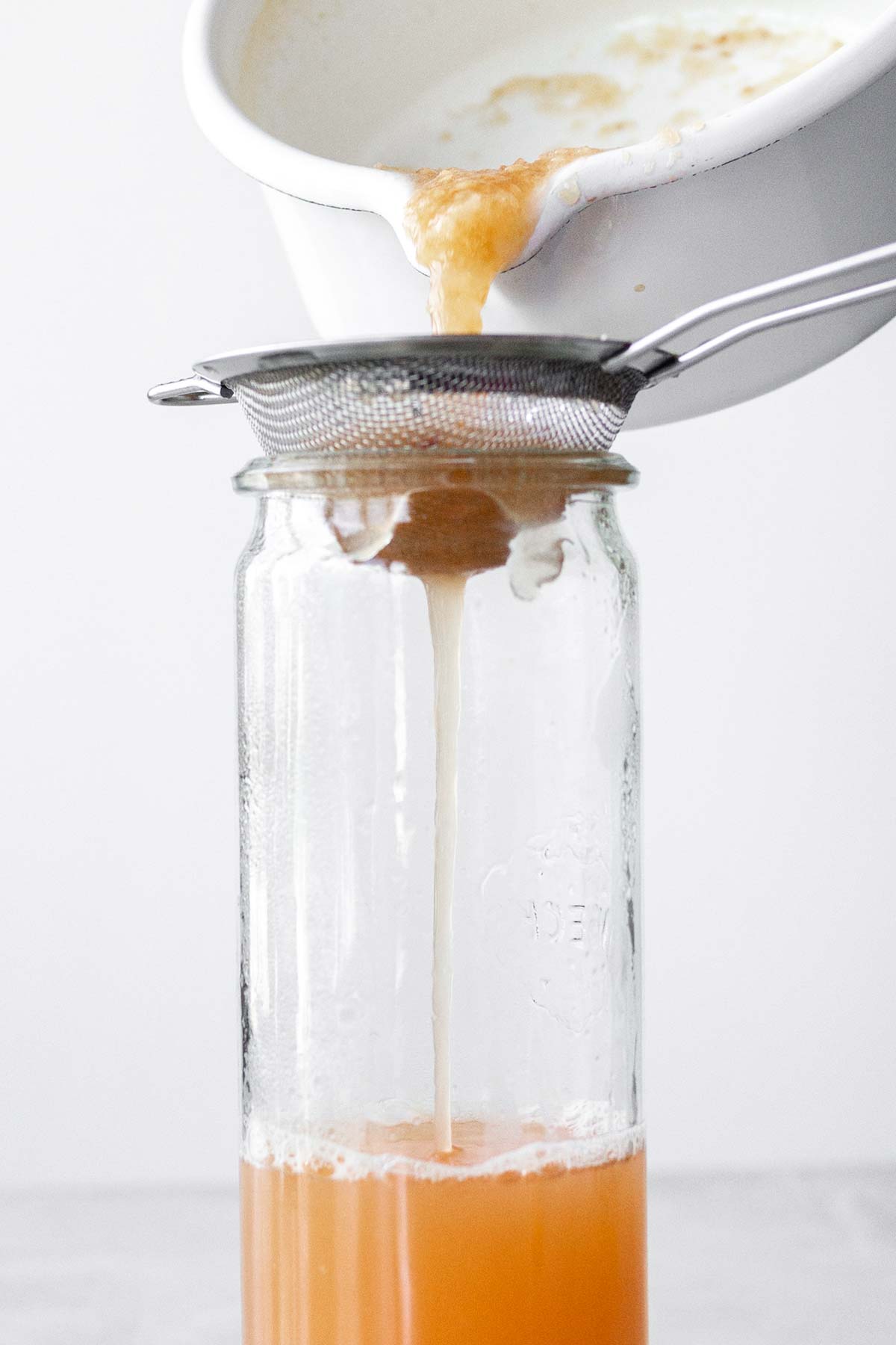 Straining peach puree into a glass container.