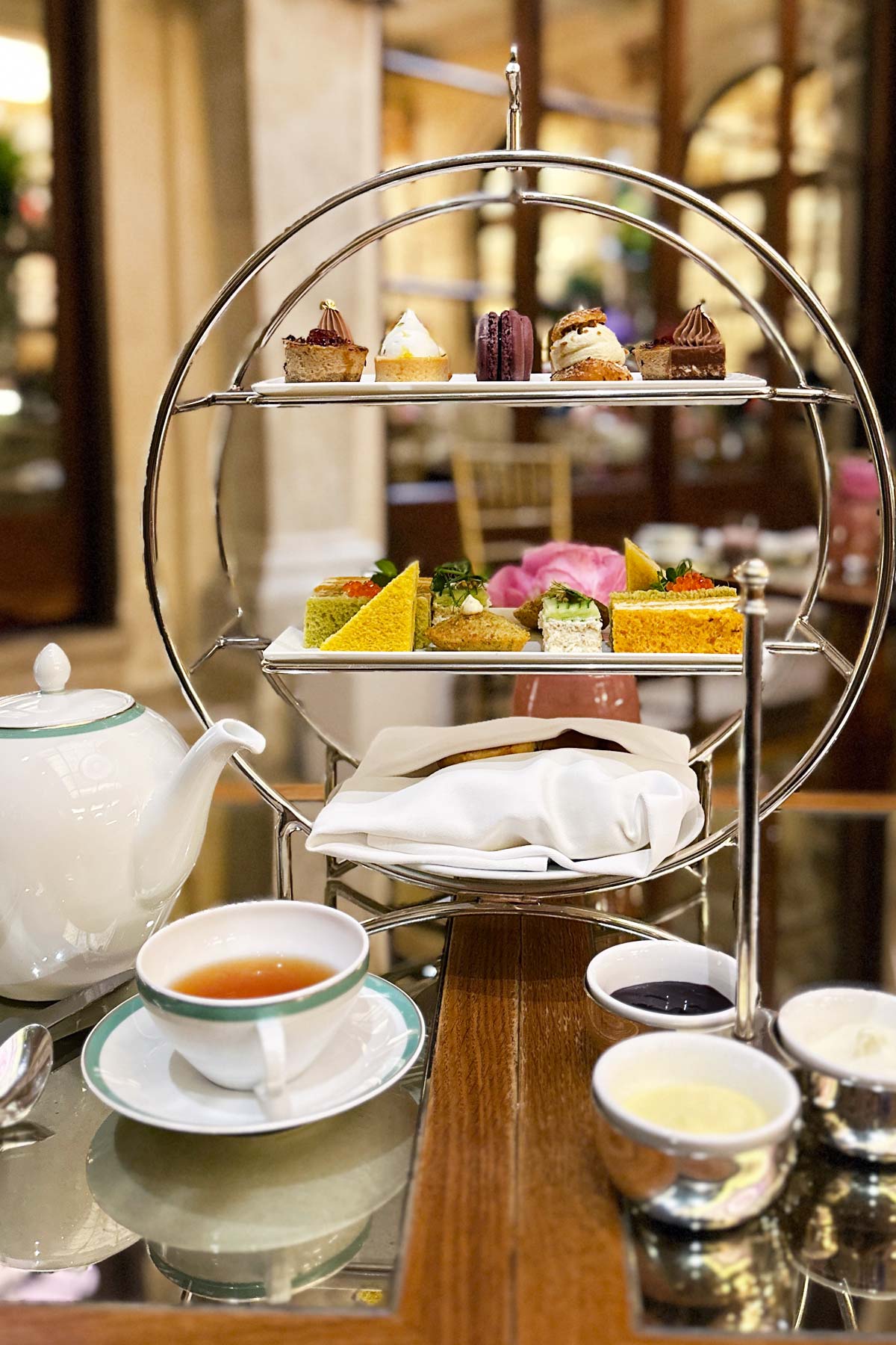 Three-tiered tray filled with food on a table with tea cup and teapot.
