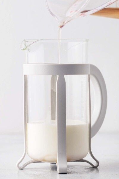 Pouring rose syrup into a French press with milk and cream.