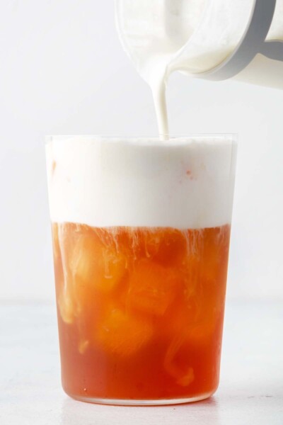 Pouring rose cold foam on top of a tea.