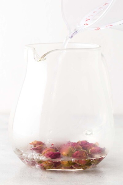Pouring hot water in a teapot with rose buds. 