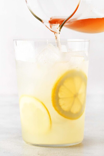 Pouring tea into a cup with lemonade, ice, and lemons. 