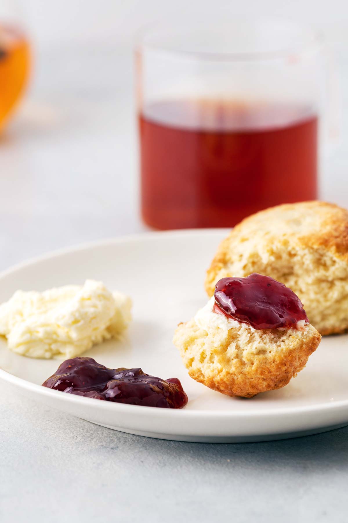 Open scone on plate with clotted cream and jam.