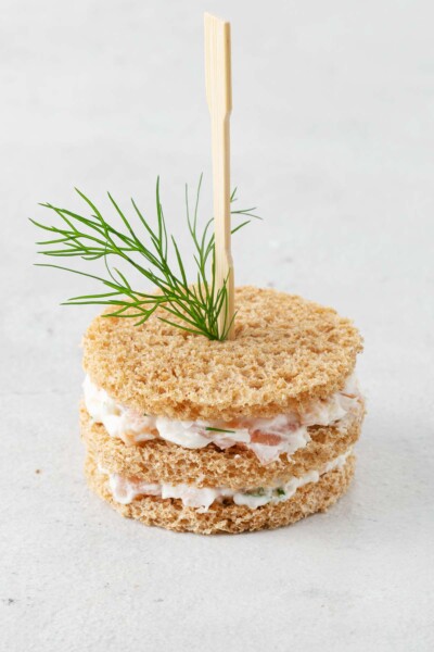 Bread cut into circles with layers of smoked salmon spread skewered with cocktail fork and fresh dill.