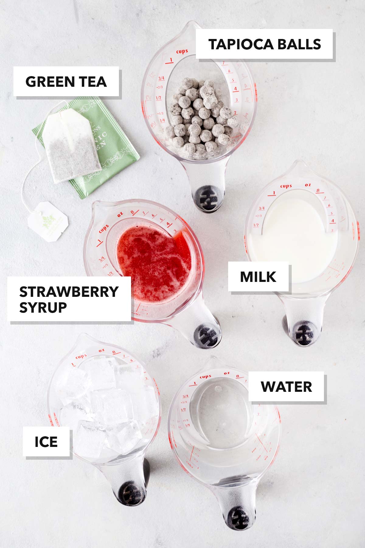 Strawberry milk tea, bubble tea ingredients with labels in measuring cups on a table.
