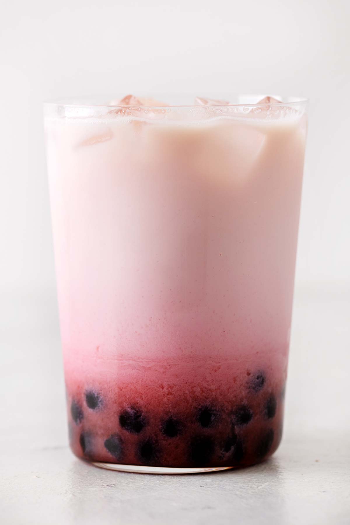Strawberry milk tea in a glass cup with boba at the bottom of the cup.