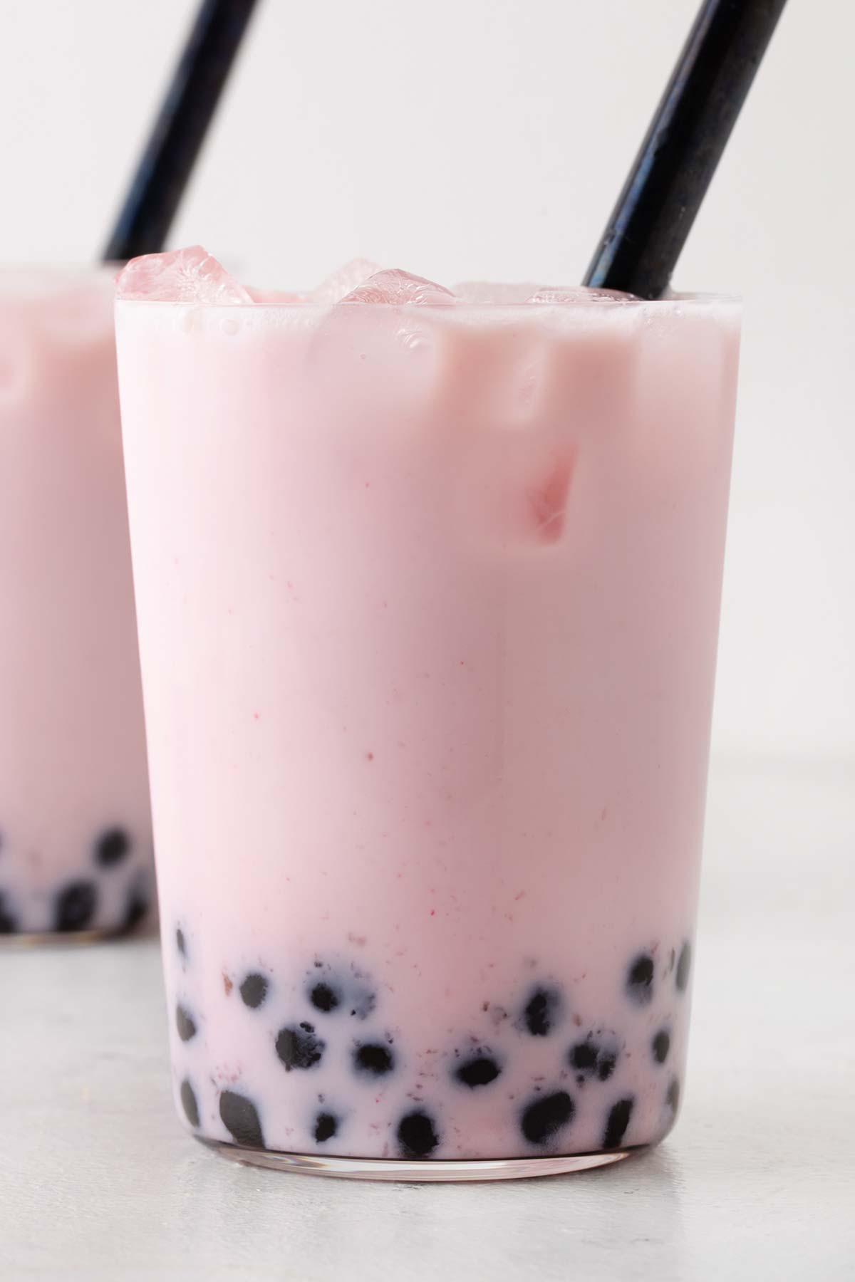 Strawberry milk tea in a clear glass with a large straw.