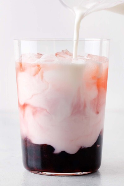 Pouring milk in a cup with green tea, strawberry syrup, ice, and tapioca balls. 