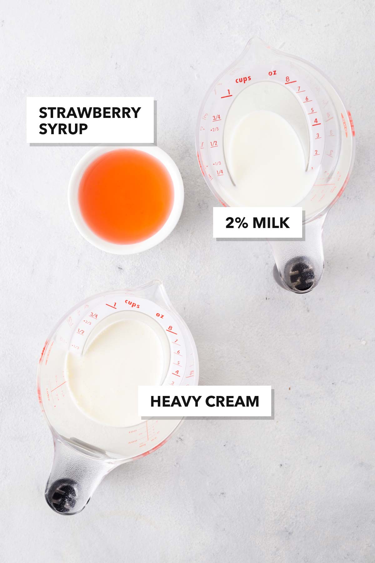 Strawberry cold foam ingredients in measuring cups on a table.