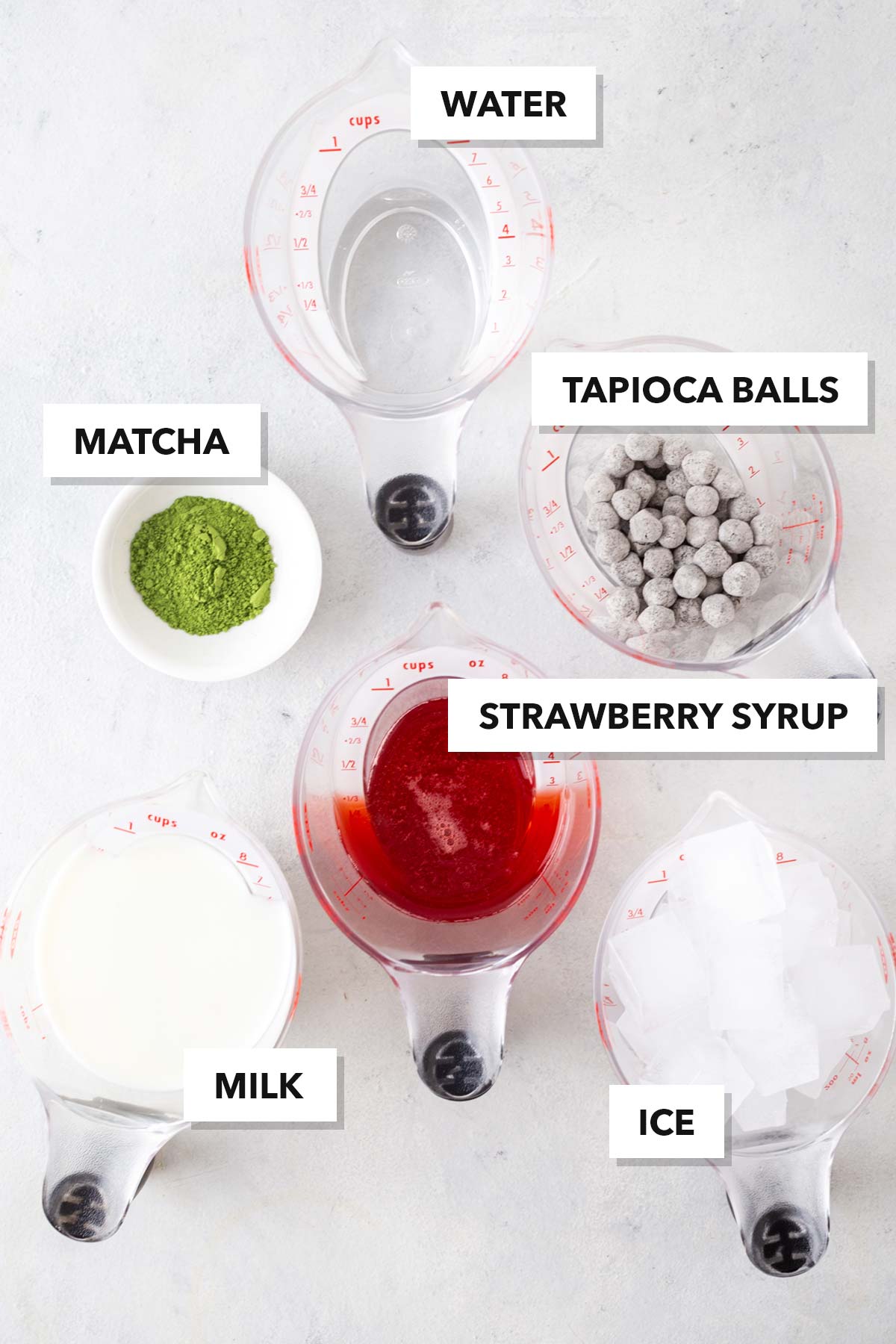 Strawberry Matcha Latte Bubble Tea ingredients on a table, labeled in measuring cups and small bowls.