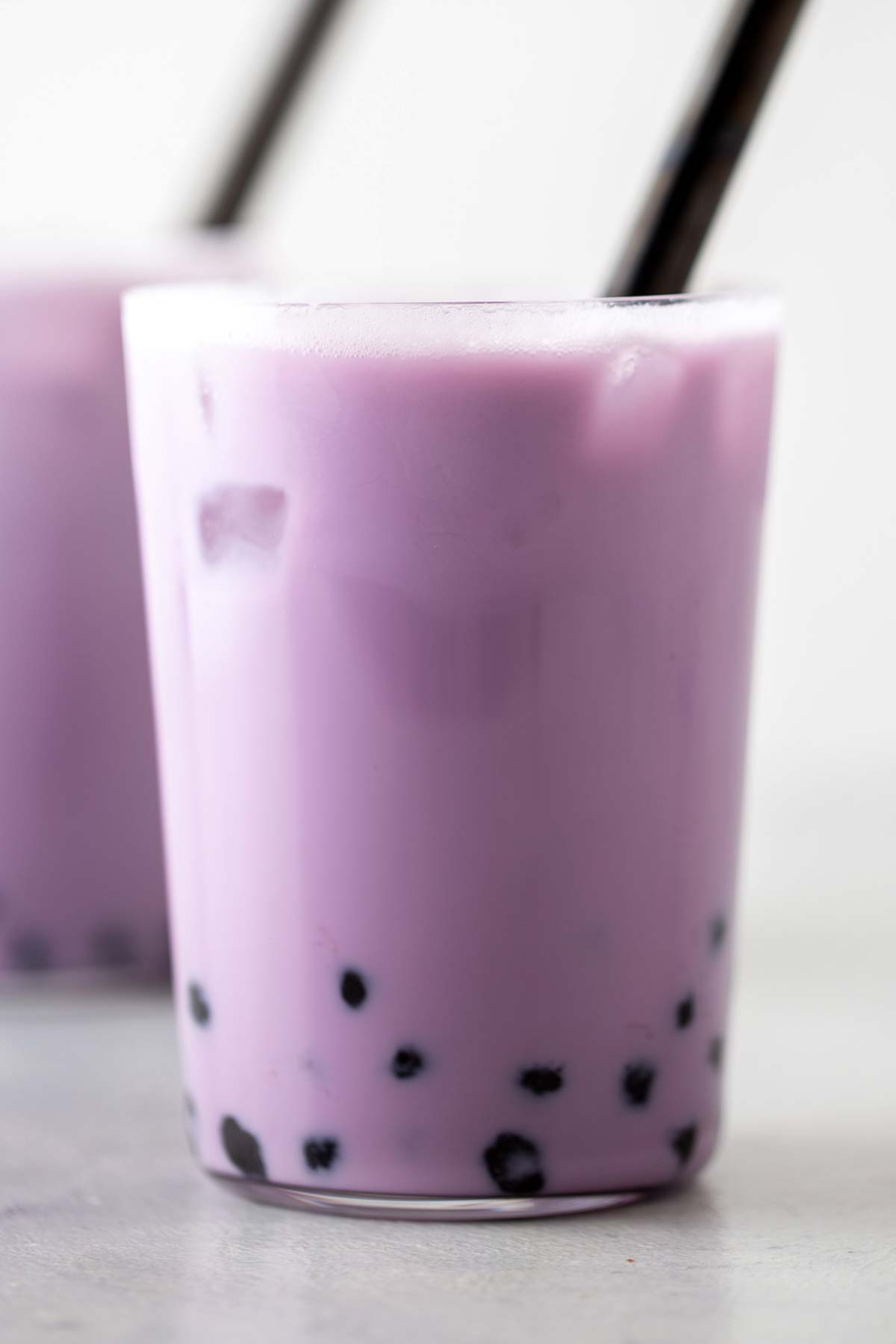 Taro bubble teas in a glass with black straws.